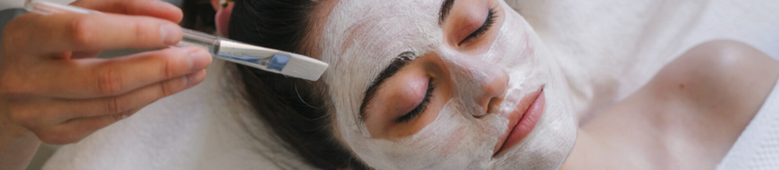Woman receiving a white facial mask applied with a brush at a spa