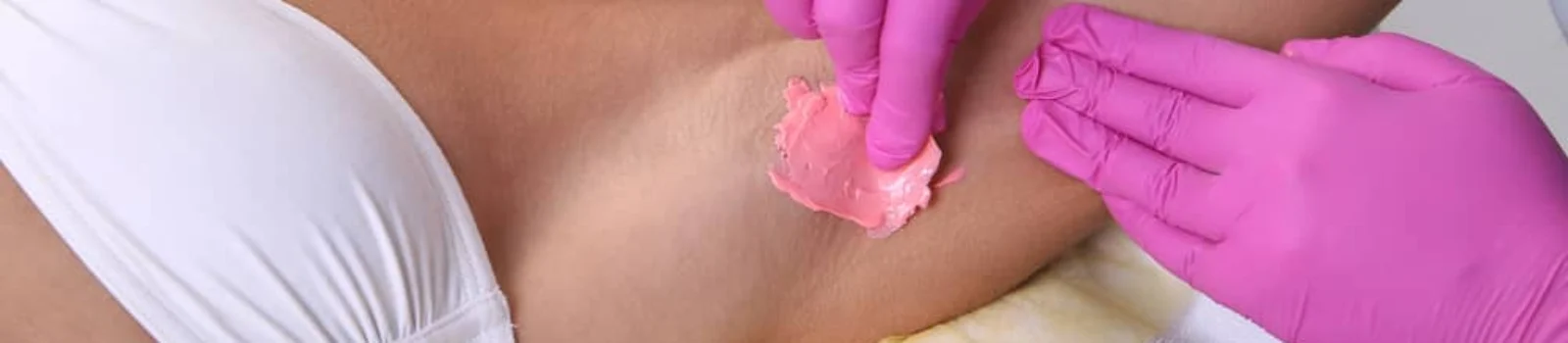 Beauty technician applies pink wax to client’s underarm for hair removal