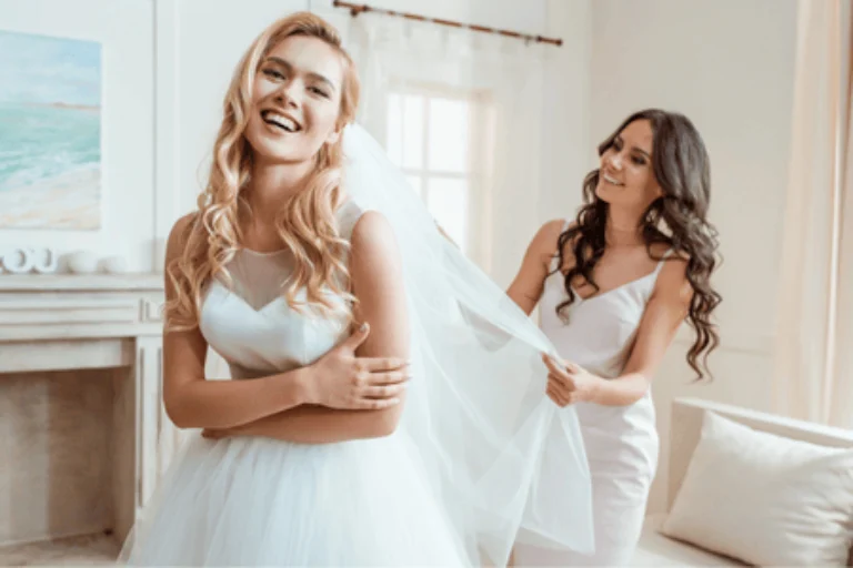 Bridesmaid helps adjust veil while ensuring bride’s bridesmaid blowout hair remains flawless and styled