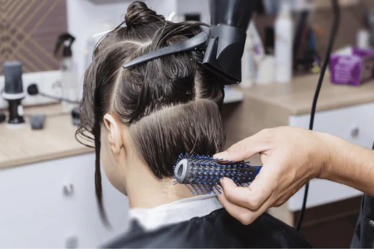 A hairstylist drying sectioned hair with a round brush, showing benefits of a blowout