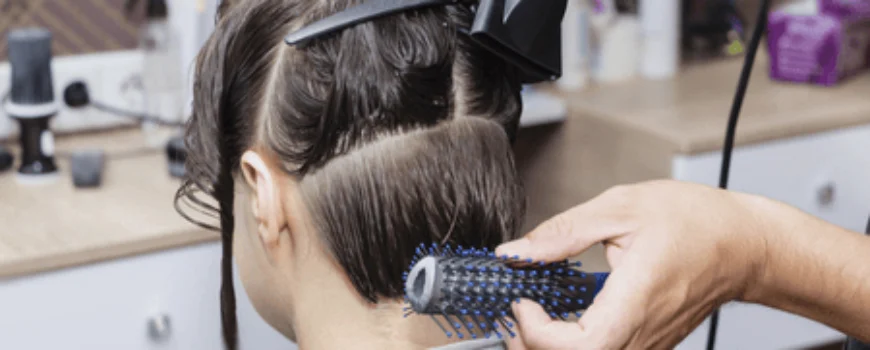 A hairstylist drying sectioned hair with a round brush, showing benefits of a blowout