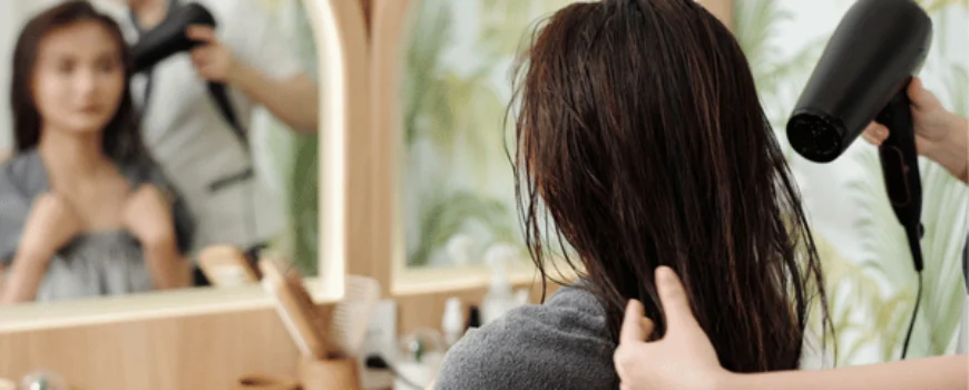 Stylist blow-dries wet hair in salon to show what does a blowout do to your hair