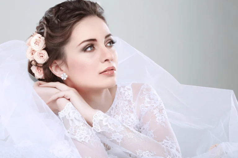 Bride in lace gown with veil and flowers gazes upward, serene portrait before wedding ceremony
