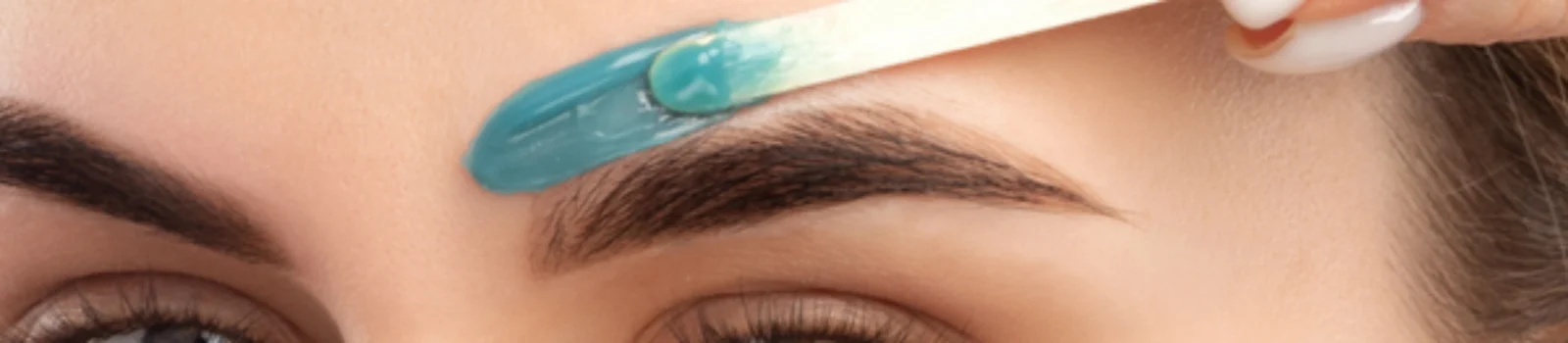 Close-up of a woman applying blue wax above her eyebrow using a wooden spatula