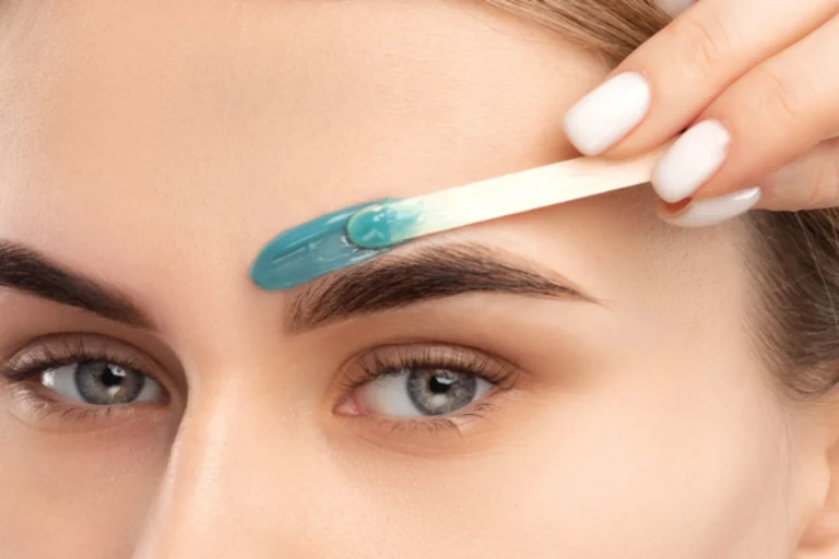 Close-up of a woman applying blue wax above her eyebrow using a wooden spatula