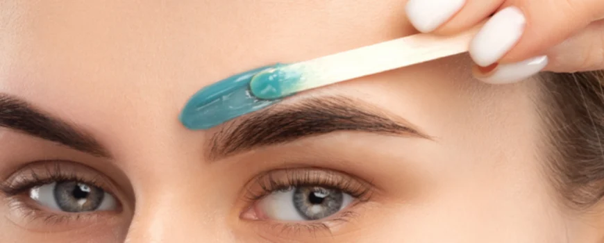 Close-up of a woman applying blue wax above her eyebrow using a wooden spatula