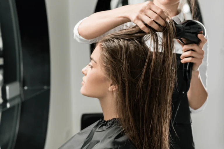 Hairstylist blow-dries client's wet hair in salon, demonstrating professional drying technique and equipment for extensions