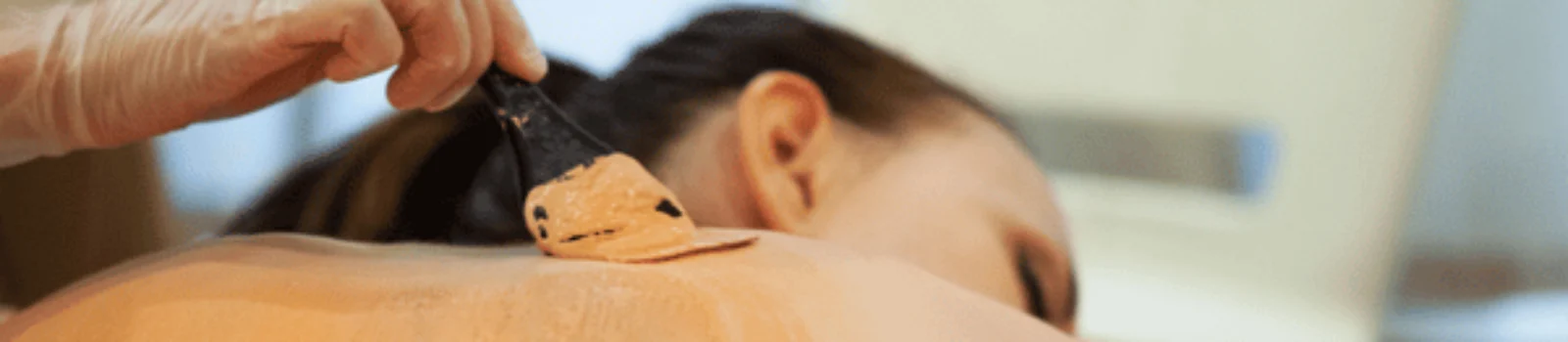 Therapist spreads warm clay mask across woman