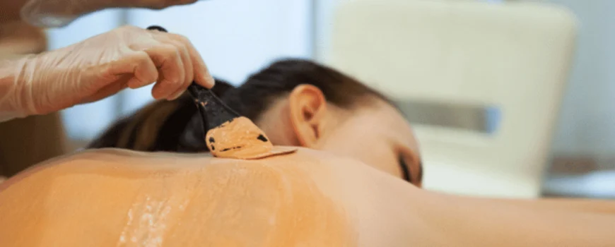 Therapist spreads warm clay mask across woman