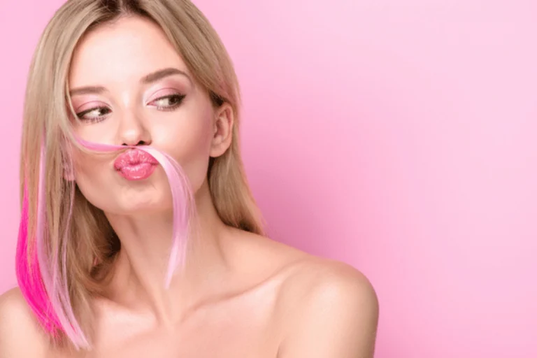 Woman puckers lips, playful pink hair strand as mustache, studio beauty portrait on pink background
