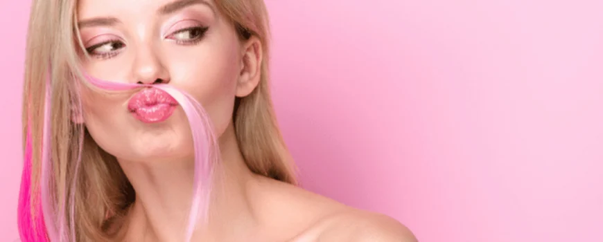 Woman puckers lips, playful pink hair strand as mustache, studio beauty portrait on pink background