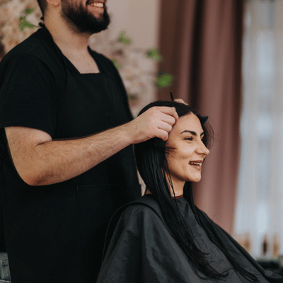 Hairdresser parts client's hair during consultation, reviewing average cost of extensions, method options and timeline