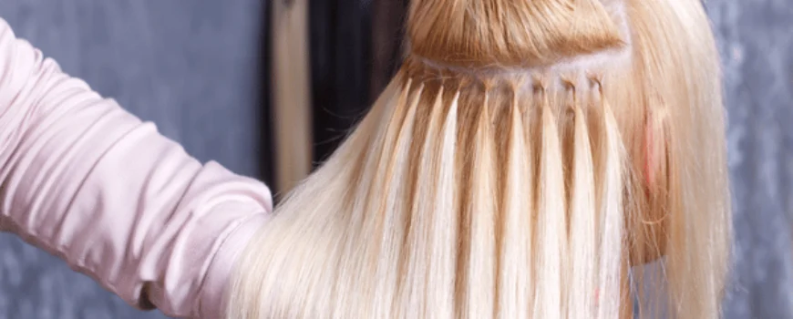 Stylist applies bonded strands during installation; explaining average cost of extensions and maintenance for clients