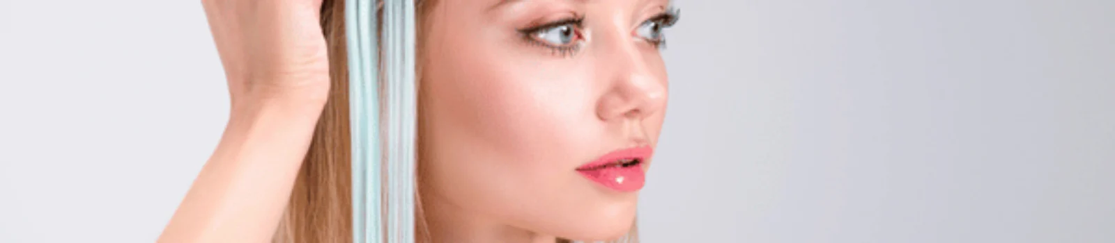 Woman holds light blue extension against blonde hair, demonstrating hair extensions services for color accents