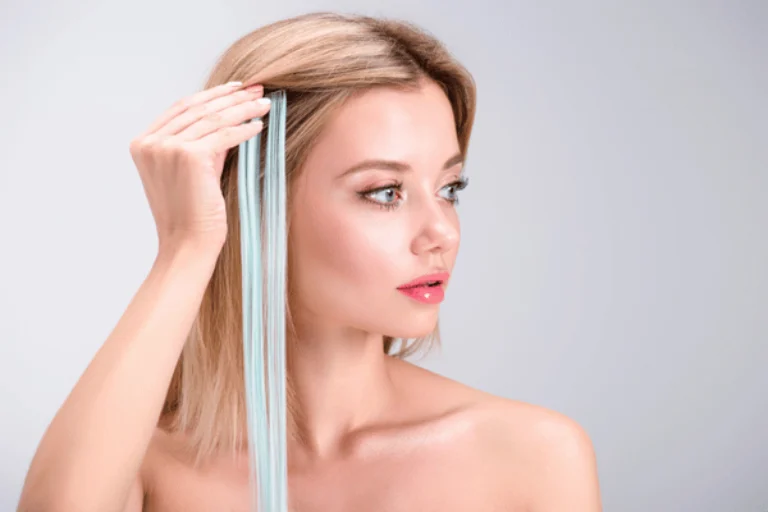 Woman holds light blue extension against blonde hair, demonstrating hair extensions services for color accents