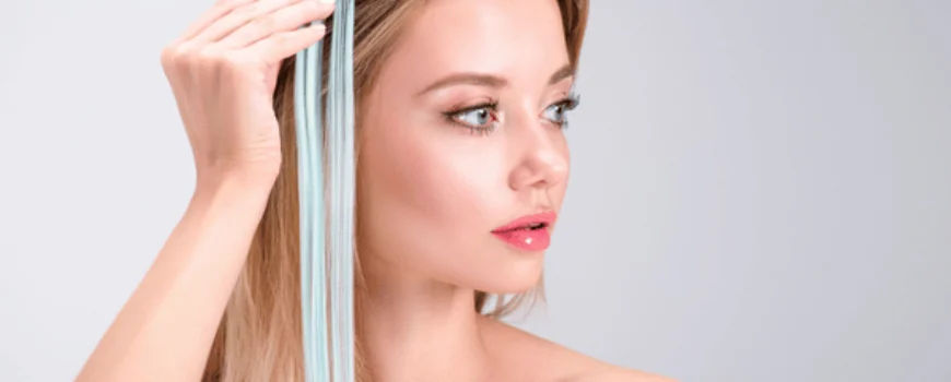 Woman holds light blue extension against blonde hair, demonstrating hair extensions services for color accents