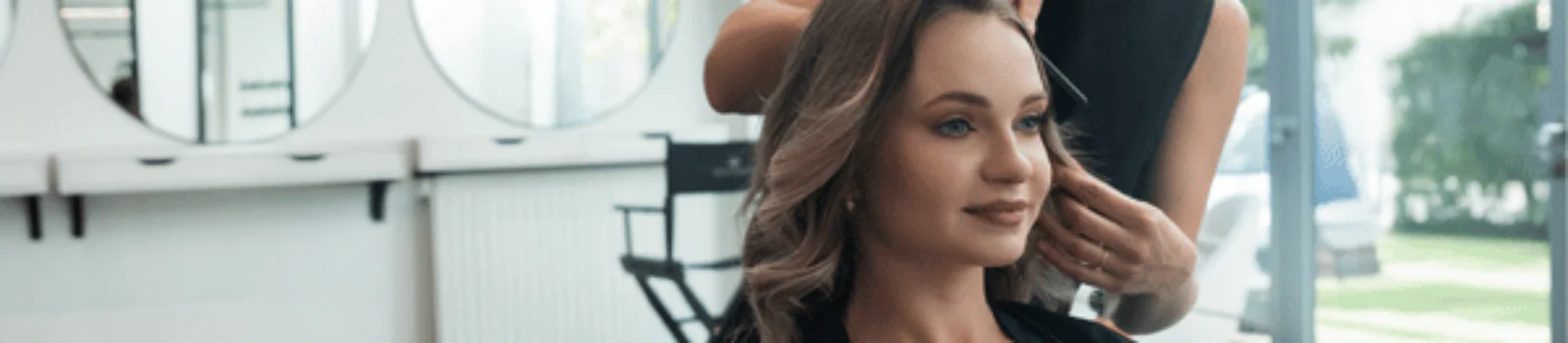 Photo shows stylist arranging client’s curled hair in salon chair, blowout with extensions service