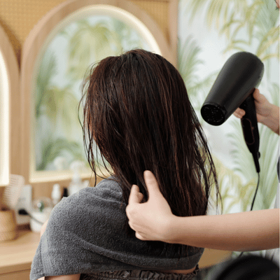 Photo shows stylist blowdrying damp hair behind client, preparing blowout with extensions result