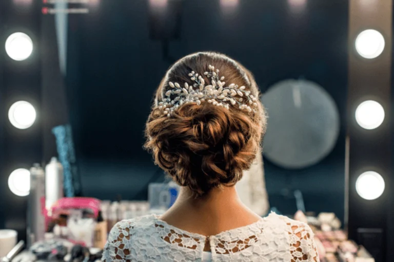 Bride shows elegant updo with jeweled comb in mirror, bridal hair and makeup prep area