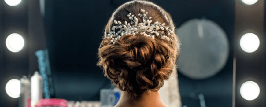 Bride shows elegant updo with jeweled comb in mirror, bridal hair and makeup prep area