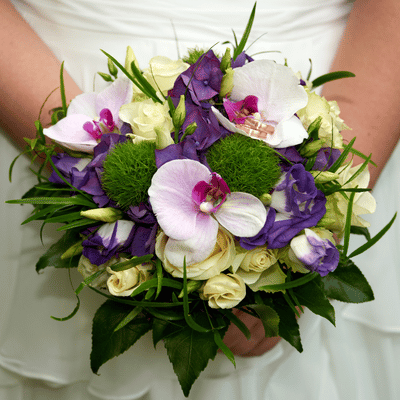 Bride holds purple and white bouquet, styled for wedding day with lash and brow services