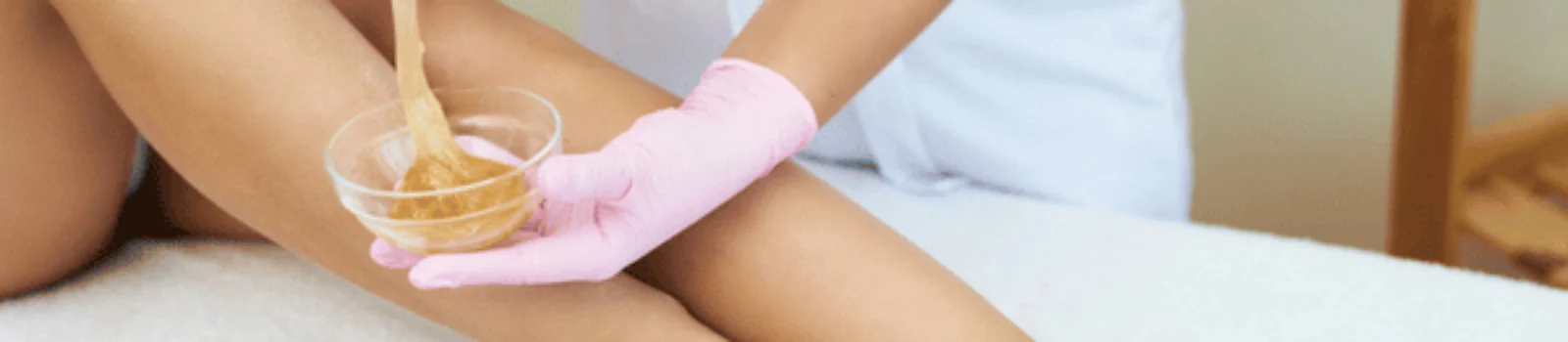 Esthetician applies warm wax to client’s legs, demonstrating body waxing in waco service process