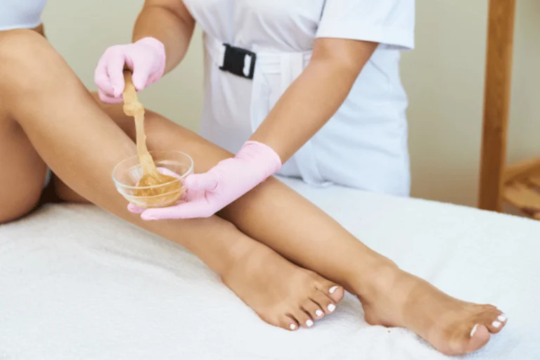 Esthetician applies warm wax to client’s legs, demonstrating body waxing in waco service process