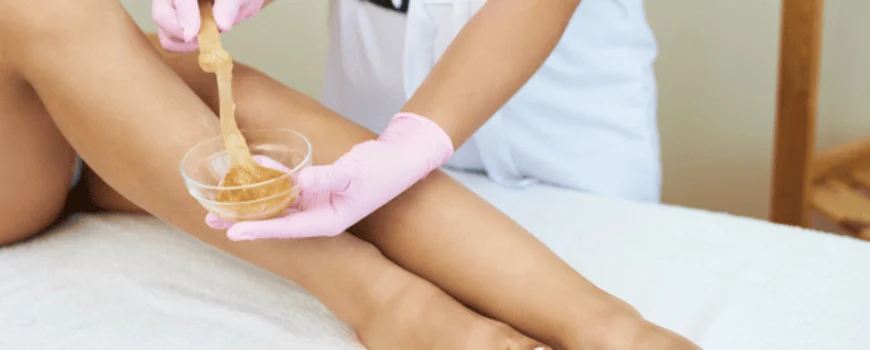 Esthetician applies warm wax to client’s legs, demonstrating body waxing in waco service process